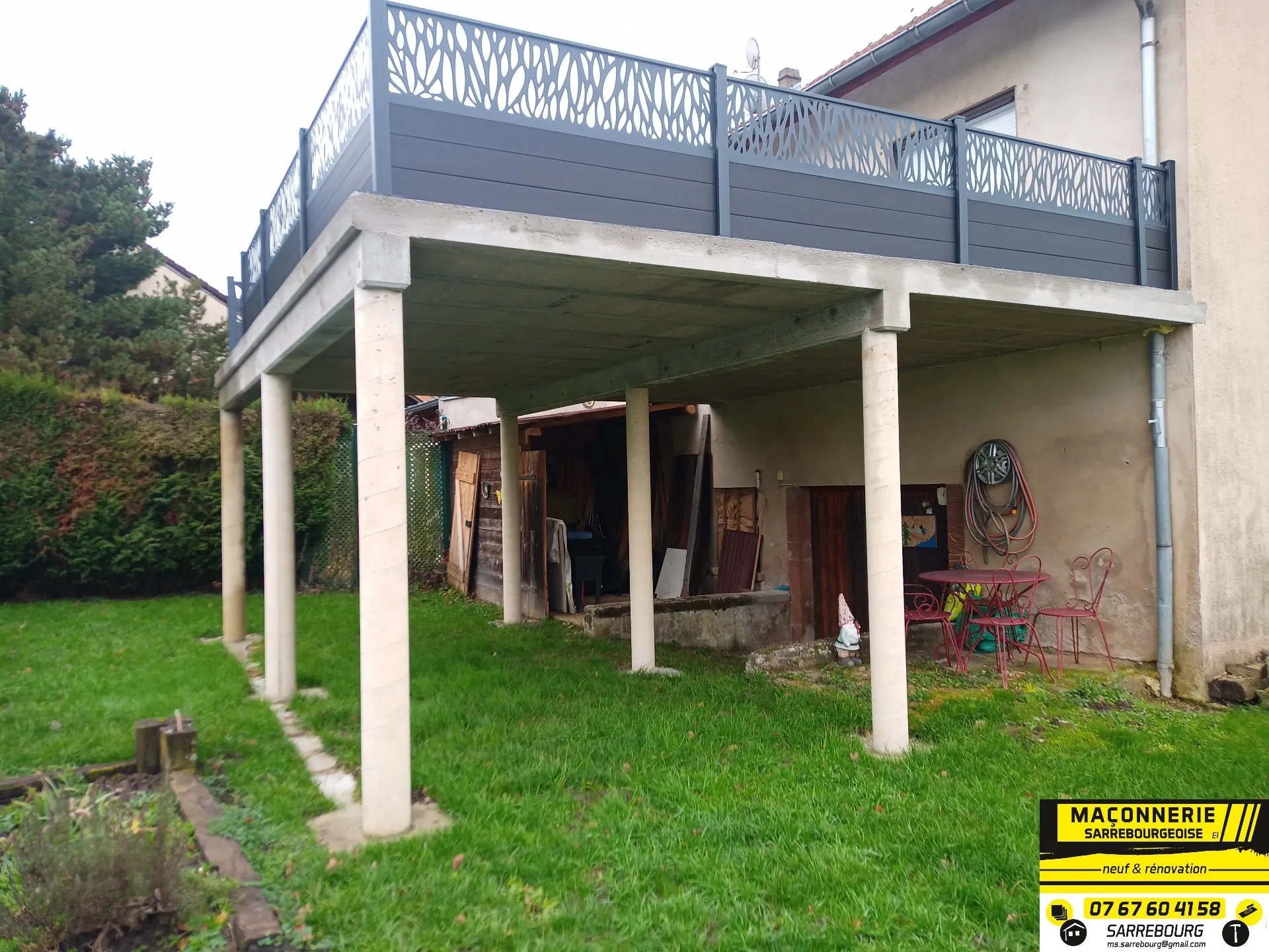 Terrasse en béton armé sur piliers, garde-corps gris, au-dessus d’un jardin