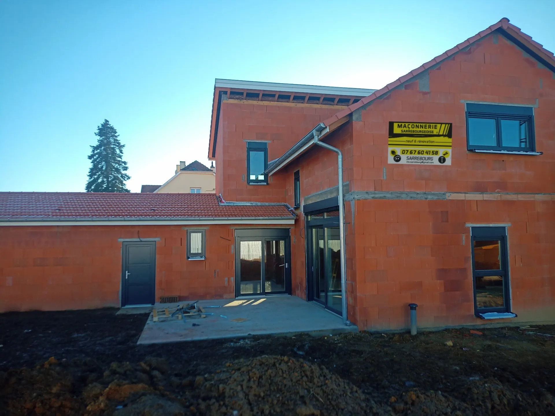 Maison individuelle à étage en briques construite par Maçonnerie Sarrebourgeoise, panneau de l’entreprise sur la façade